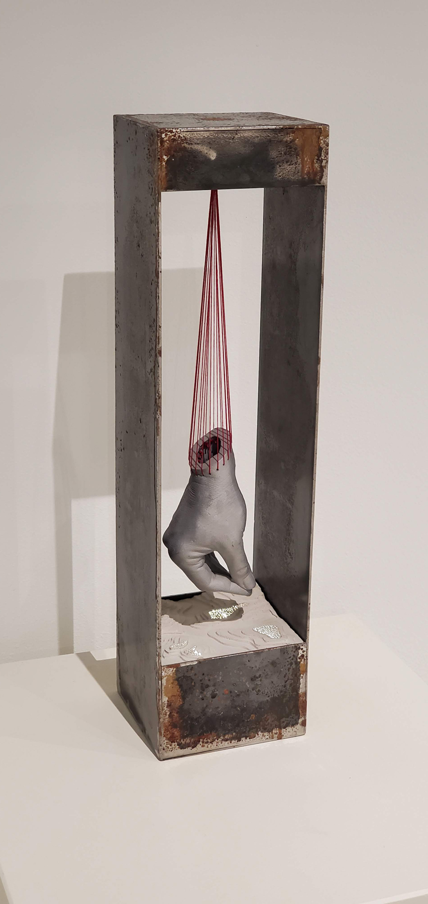 tall rectangular frame with a hand dangling from red string