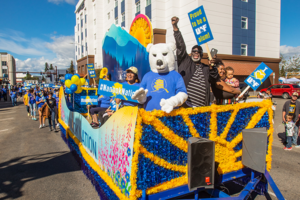 Nook is flanked by alumni Ray Alda ’21, left, and Darryl Lewis ’88, right, while waving at spectators from UAF’s parade float during the 2022 Golden Days celebration. UAF photo by Eric Engman.