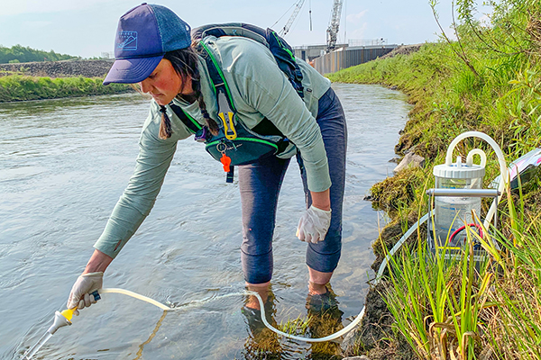 Maggie Harings uses a portable filtration device in June 2022 to collect salmon DNA in the Chena River near the Chena River Lakes Flood Control Project's Moose Creek Dam. Photo by Erik Schoen.