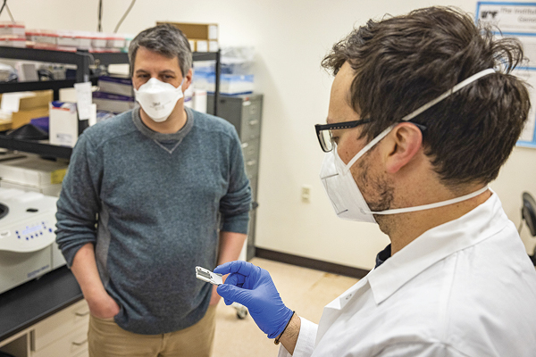 Associate professor Devin Drown, left, discusses a flow cell with Logan Mullen ’17, who works in the Genomics Core Lab.. UAF photos by Leif Van Cise.