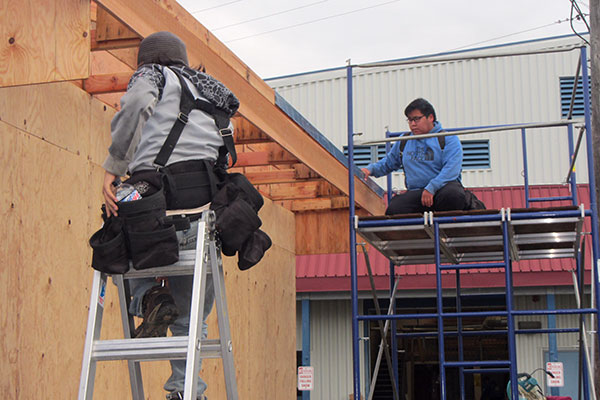 Construction trades students on scaffolding and ladders working on a wooden structure