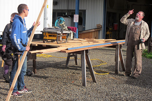 An instructor addresses a pair of construction trades students holding lumber