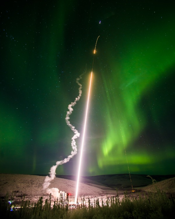 Rocket launch against an aurora filled night sky at Poker Flat Research Range