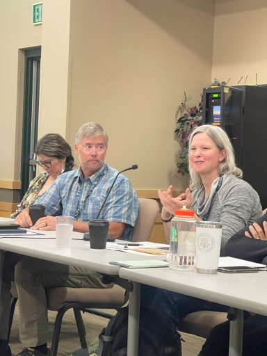 Three people have a discussion at a table in a conference room.