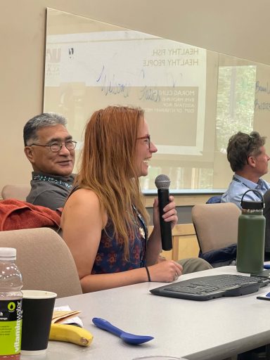 Three people have a discussion at a table in a conference room.