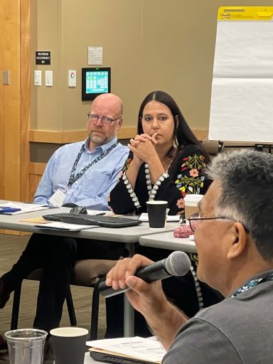 Three people have a discussion at a table in a conference room.