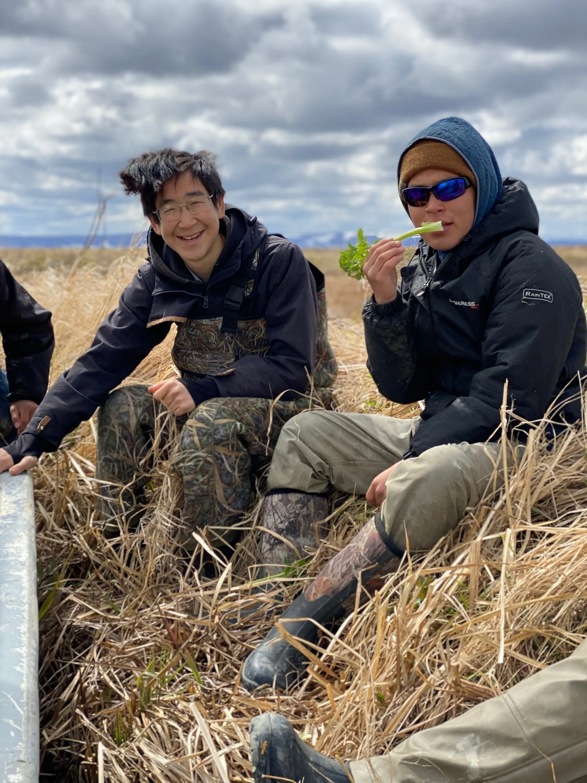 Two people sit in a field and smile at the camera