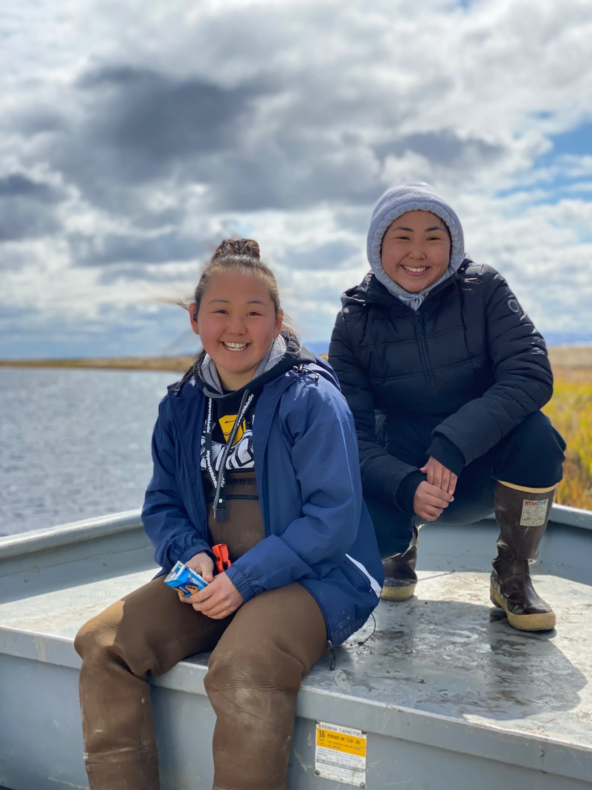 Two people sit in the back of a boat and smile at the camera