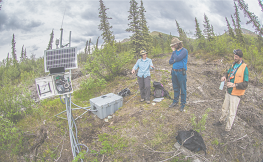 Three people stand on a tundra landscape with research equipment