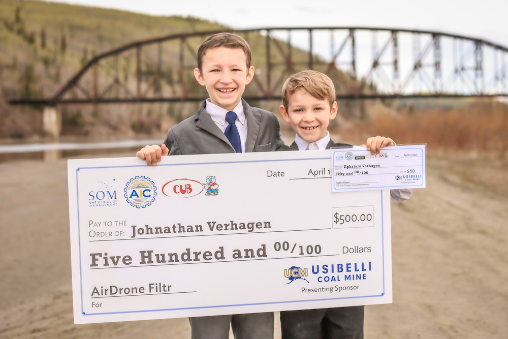 two young brothers hold up a first-place check for $500 in front of a bridge