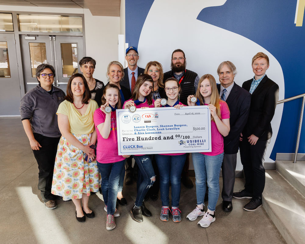 Four girls wear pink holding up giant check with university and community officials