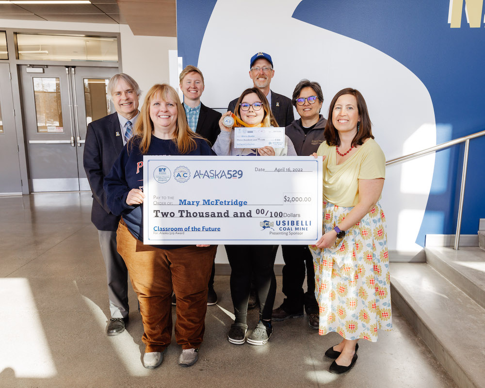 Teacher stands with her student and university officials holding giant check