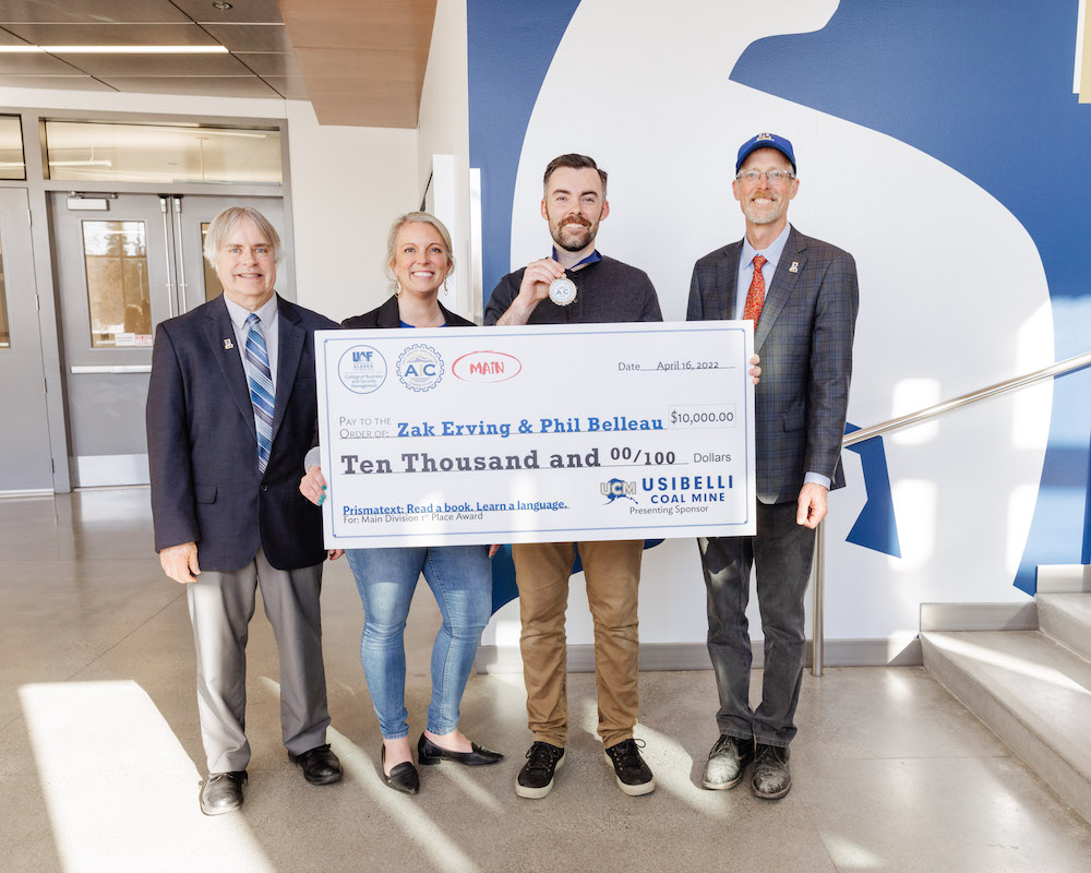 Man holds up 1st place medal and giant check in between three professionals
