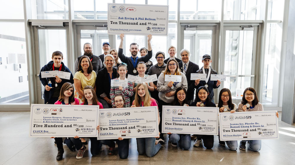 Big group of kids, adults and teachers take group photo holding up 5 giant checks and smaller awards