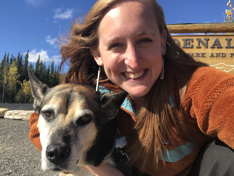 woman takes selfie with dog in front of Denali national park sign