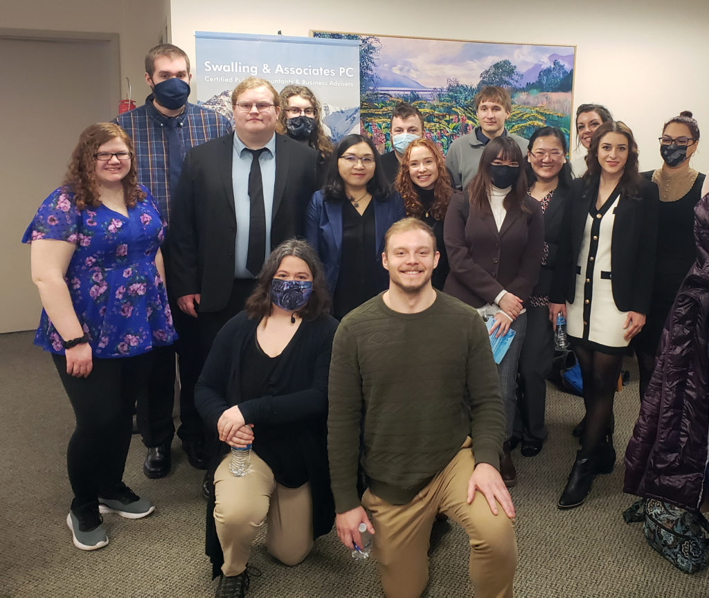 fifteen students take group photo with professionals in semi professional clothing. six are wearing masks