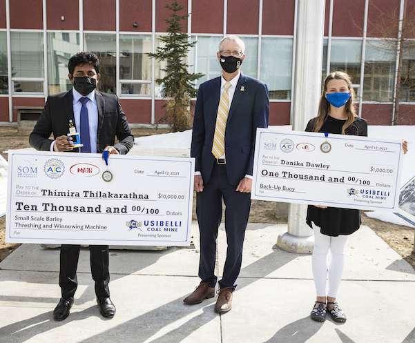 man and woman stand outside with the UAF chancellor holding giant checks. all are wearing masks during the COVID 19 pandemic.