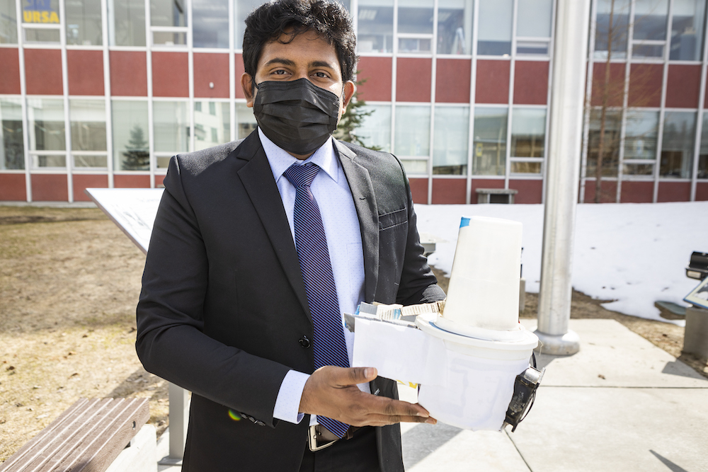 man wearing mask holds up prototype of invention