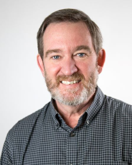 Man with dark brown hair and beard smiles in a headshot