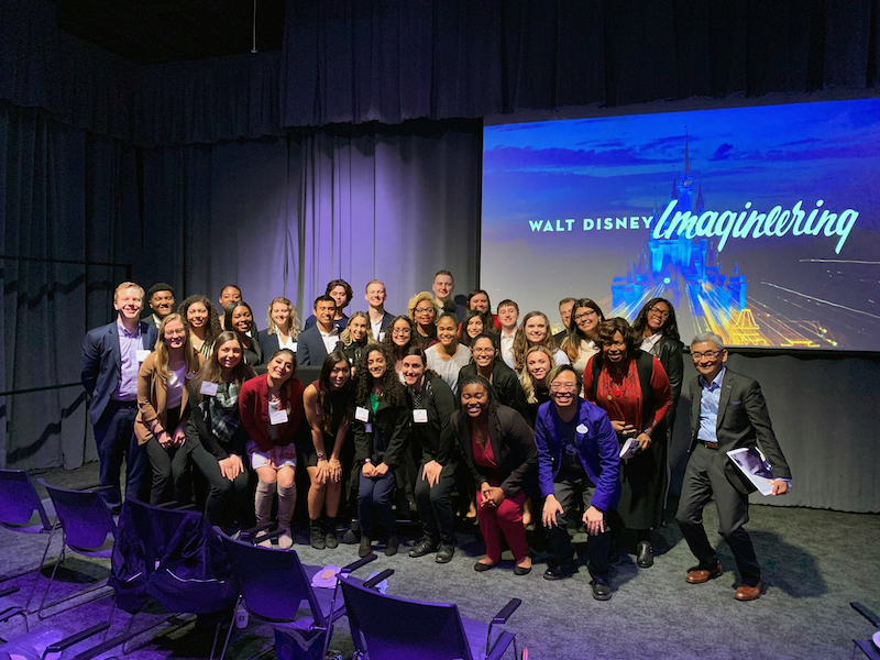 group of about 20 students take photo in front of screen that reads Walt Disney Imagineering
