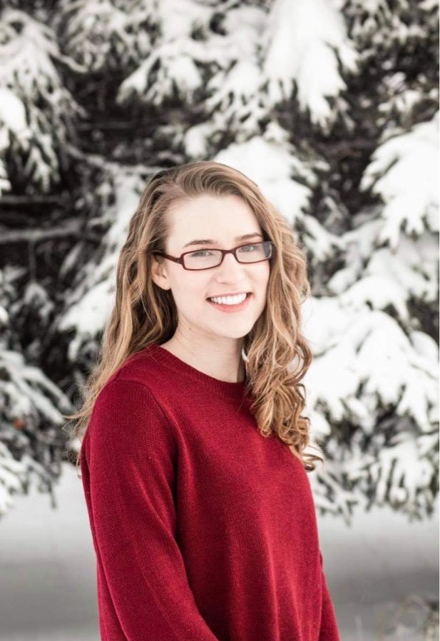 girl in red sweater smiles with snowy trees in the background