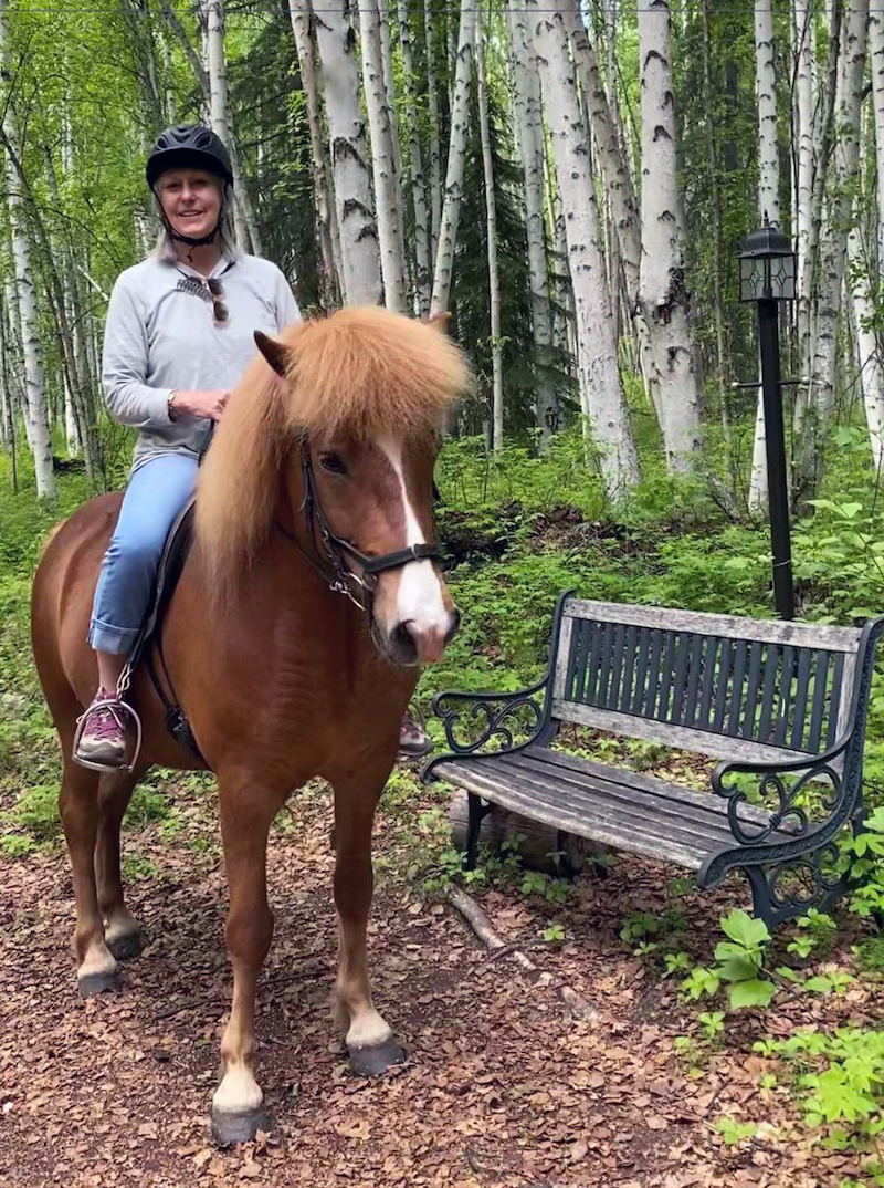 Woman, smiling, on horseback in a woodland area