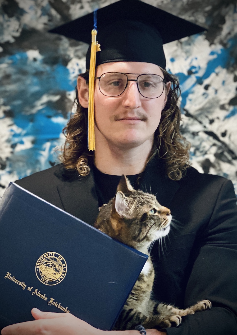 man in cap and gown poses with cat and diploma at graduation 