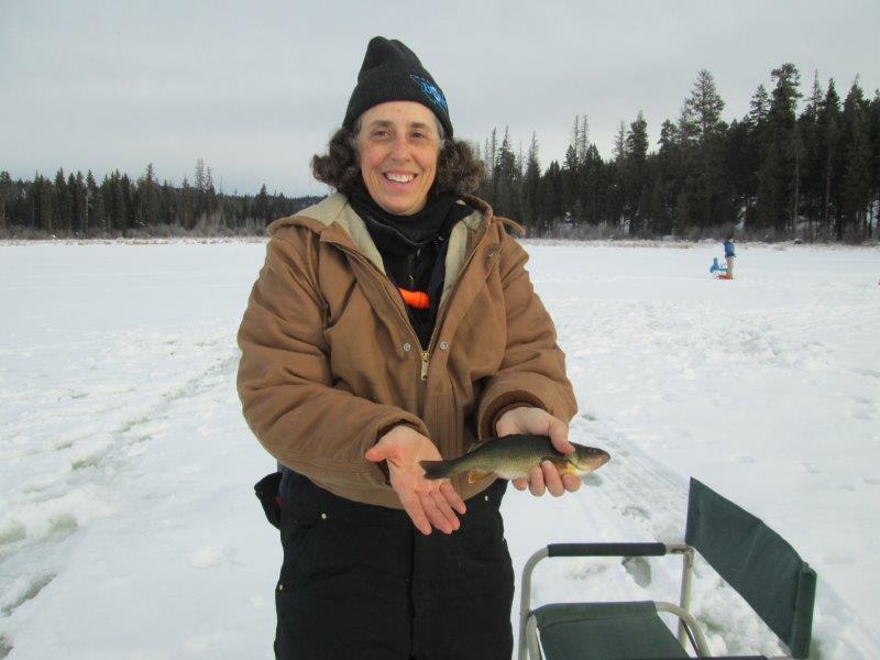 woman holds a fish that she has caught on frozen lake 