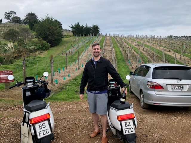 man stands with scooter in front of vineyard