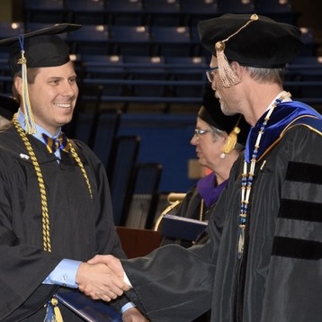 man shakes hand with an official on stage at university graduation