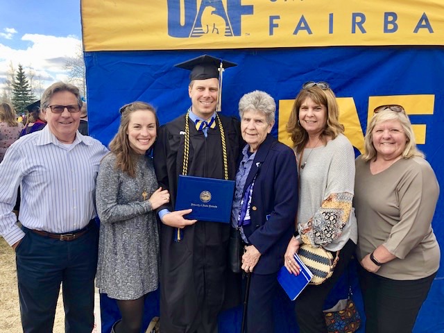 man wears regalia and poses with family outside at the UAF graduation