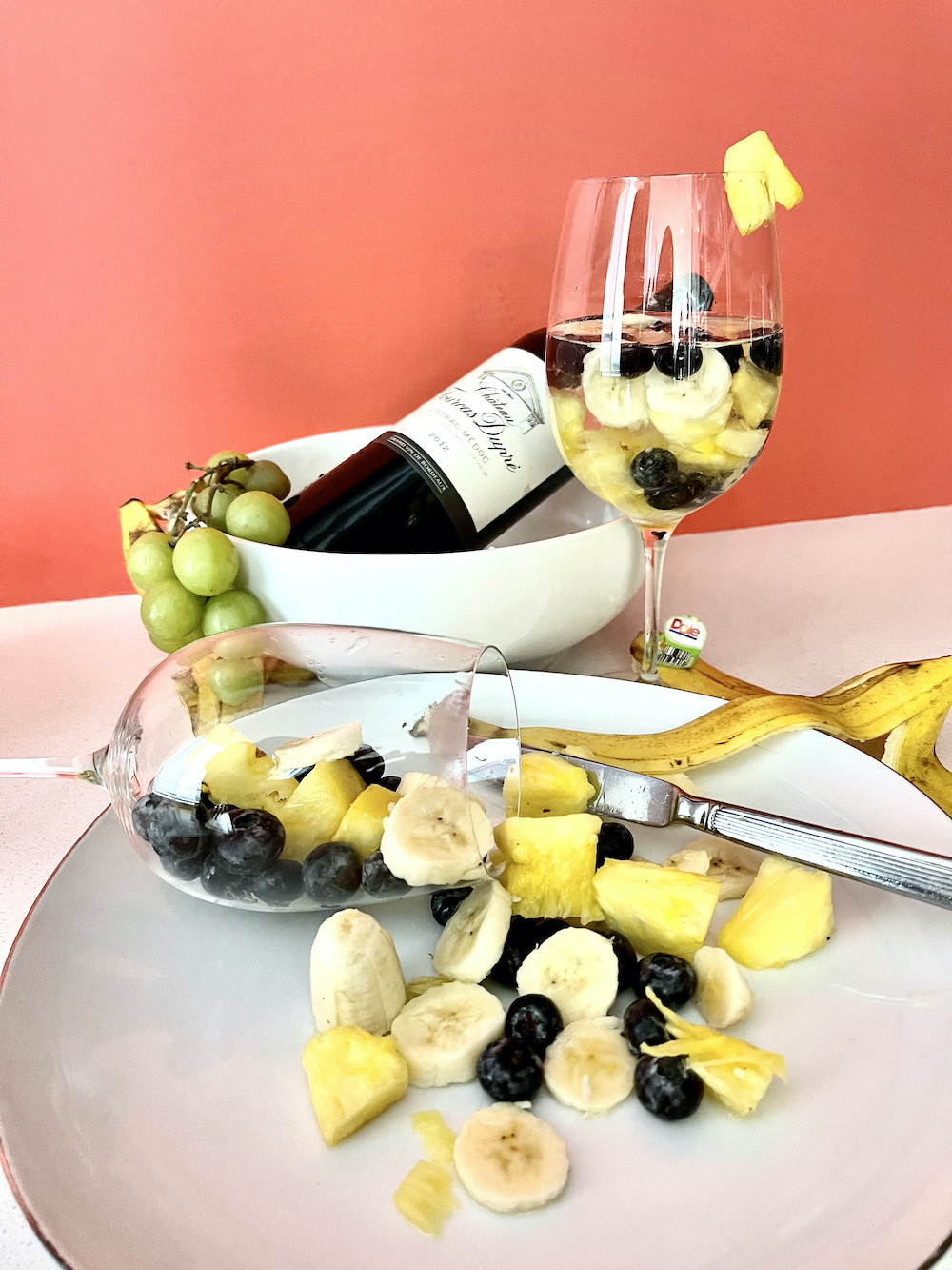 wine glass and bowl of pineapple and blackberries in front of a peach colored wall