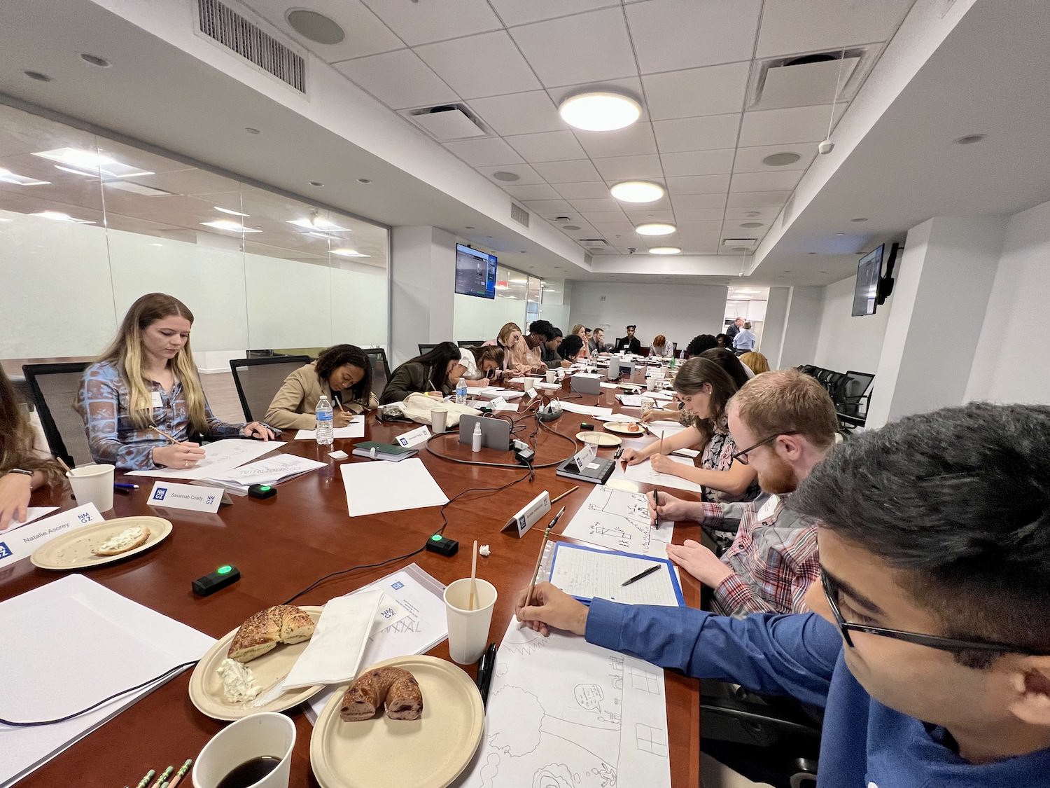 students take notes at conference table while having bagels and brunch