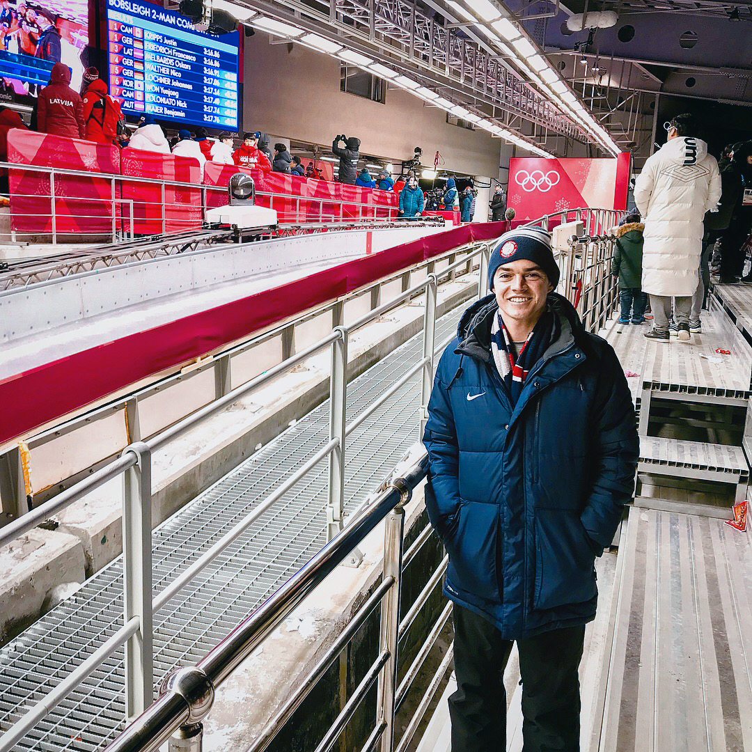Man smiles in front of the Olympic bobsled track