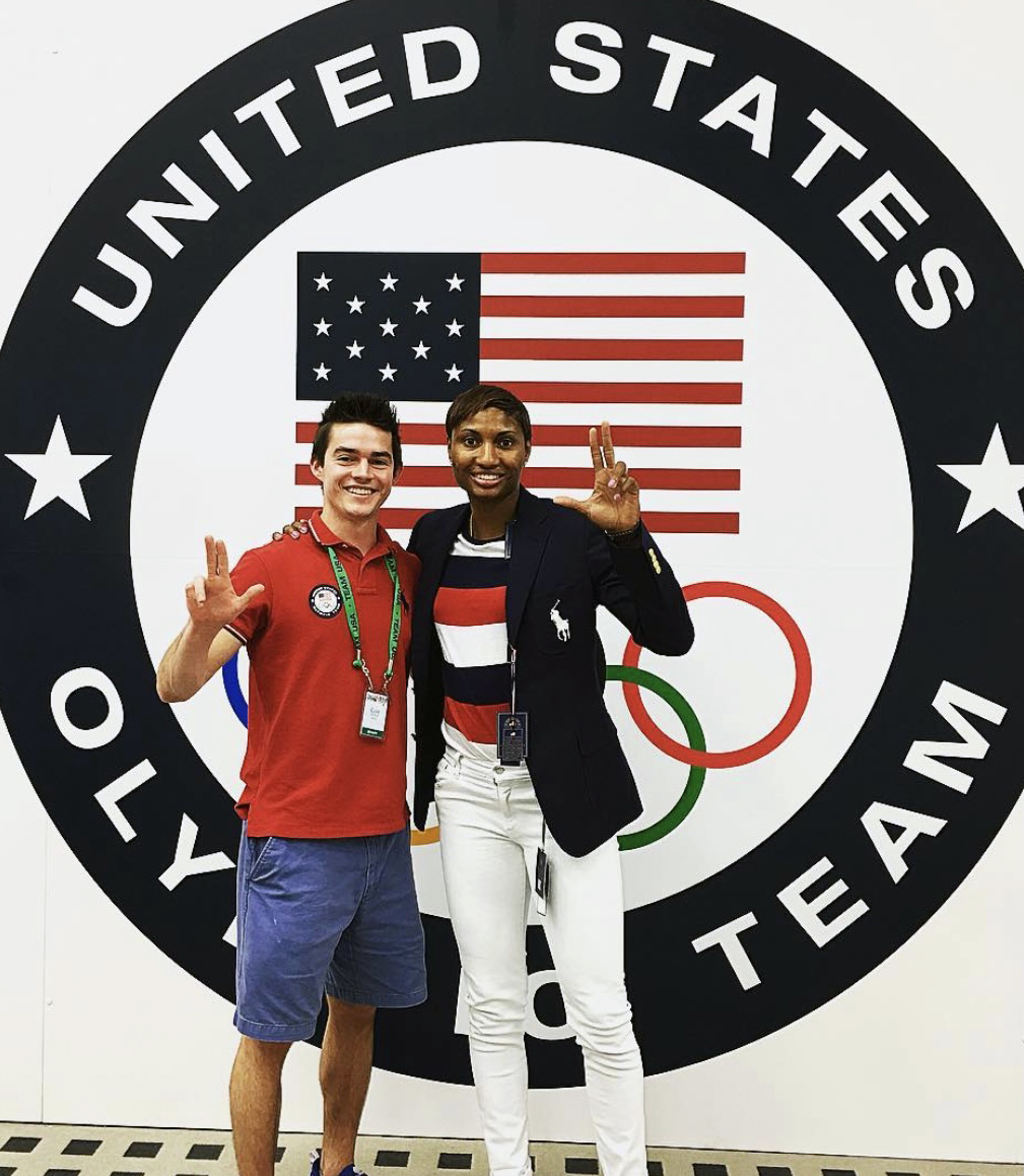 Man stands with woman, an Olympic Gold Medalists in front of United States Olympic Team logo