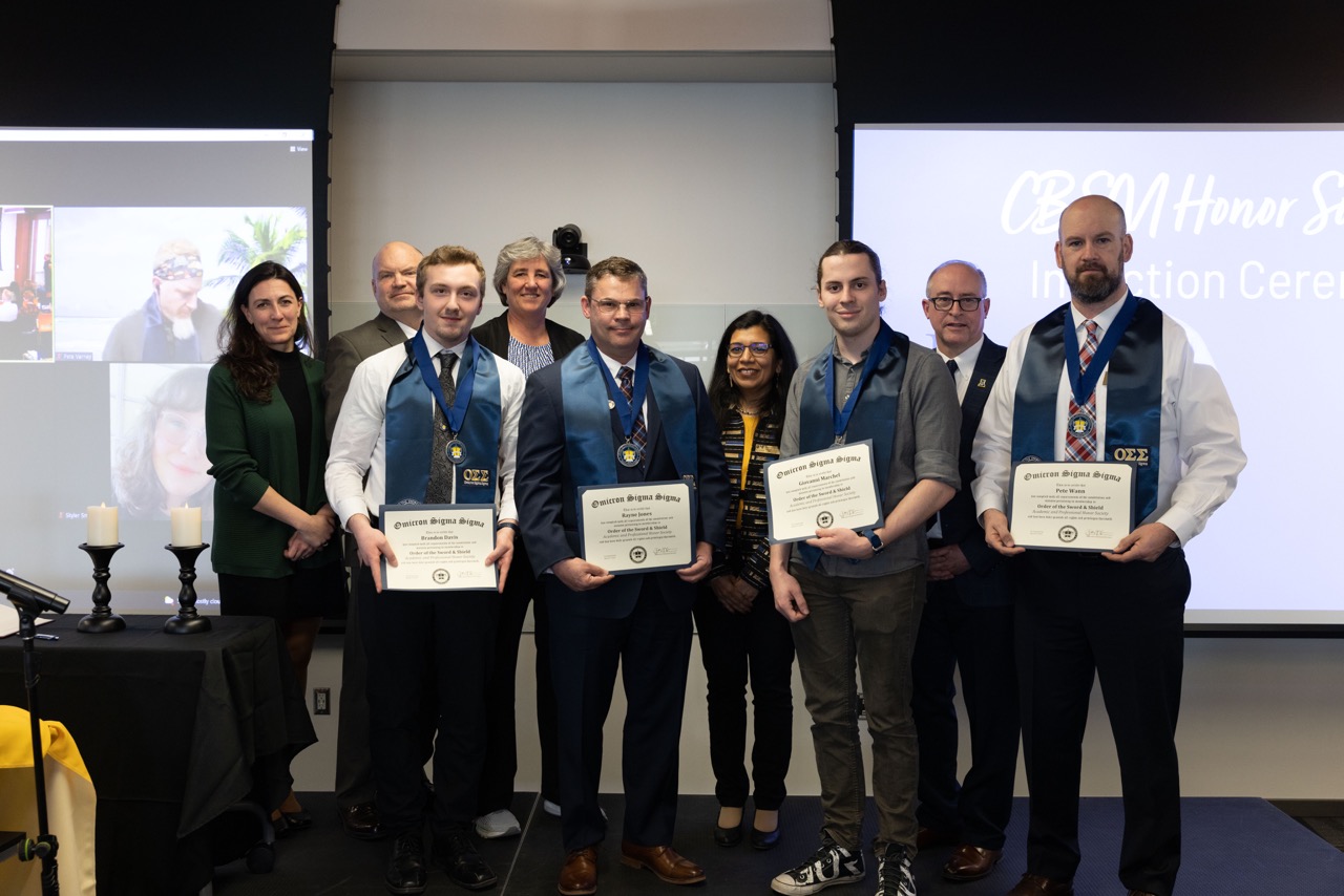 students stand wearing navy blue sashes holding certificates with university officials