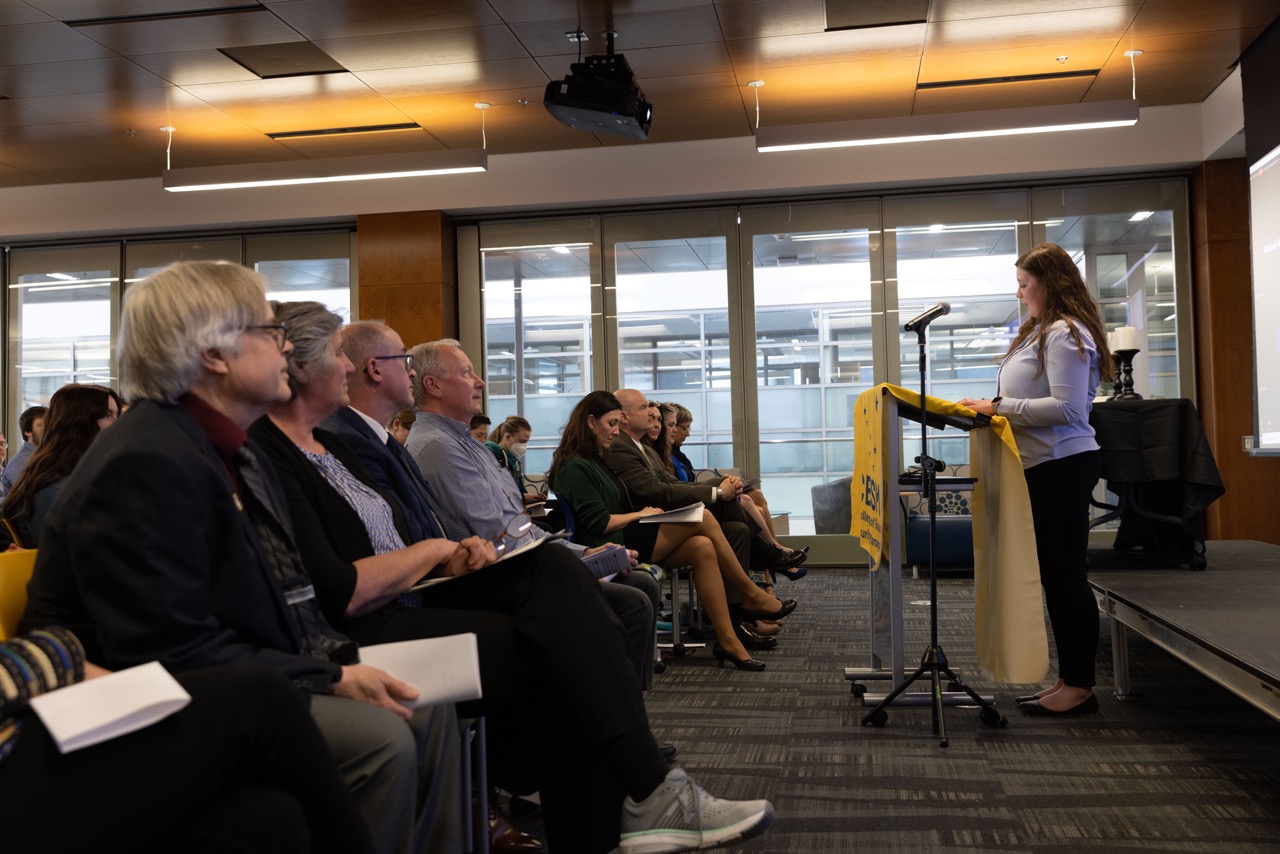 side shot of woman delivering speech behind a podium to audience