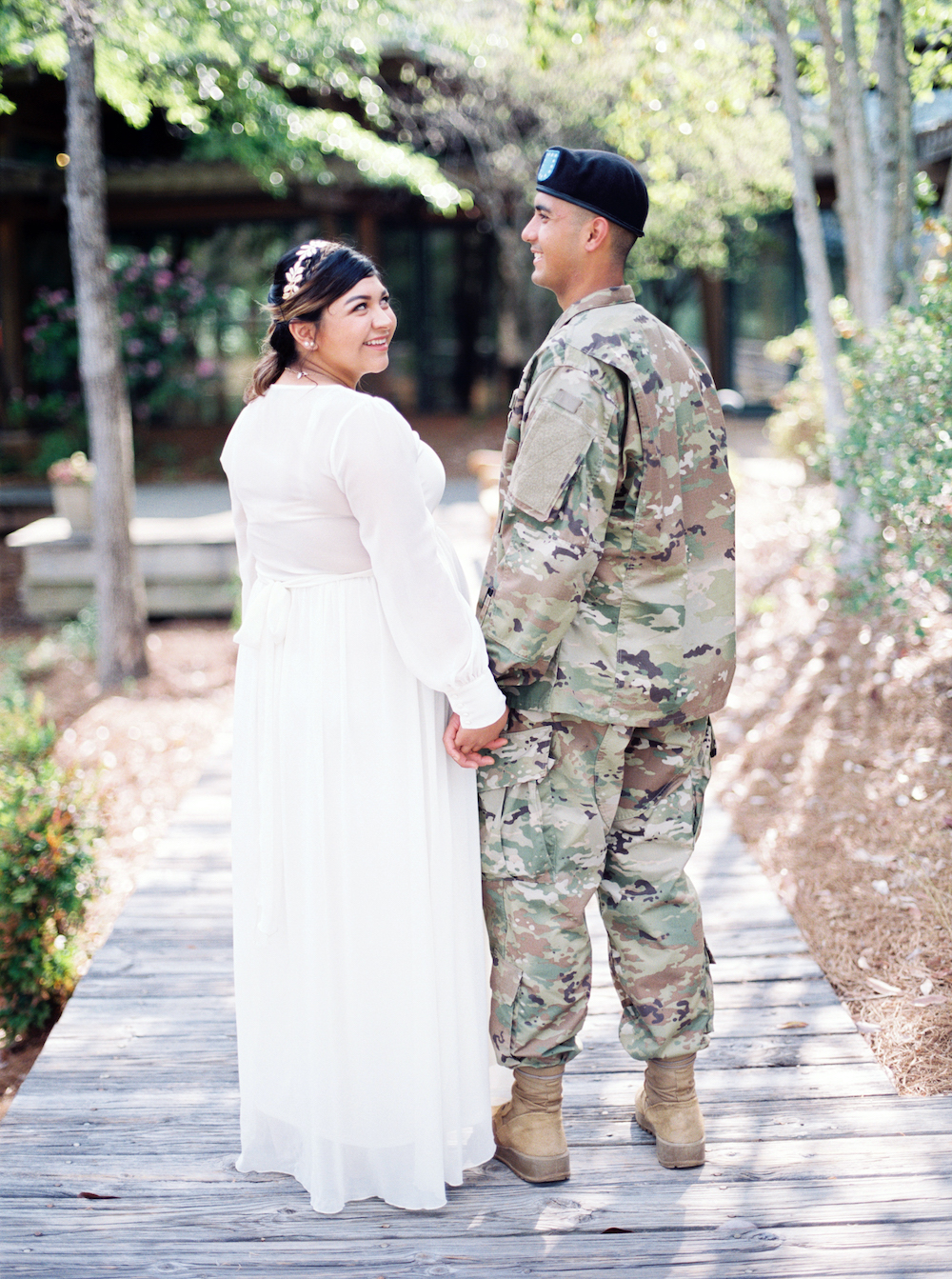 bride in white wedding dress and groom in U.S. Army uniform hold hands on a bridge