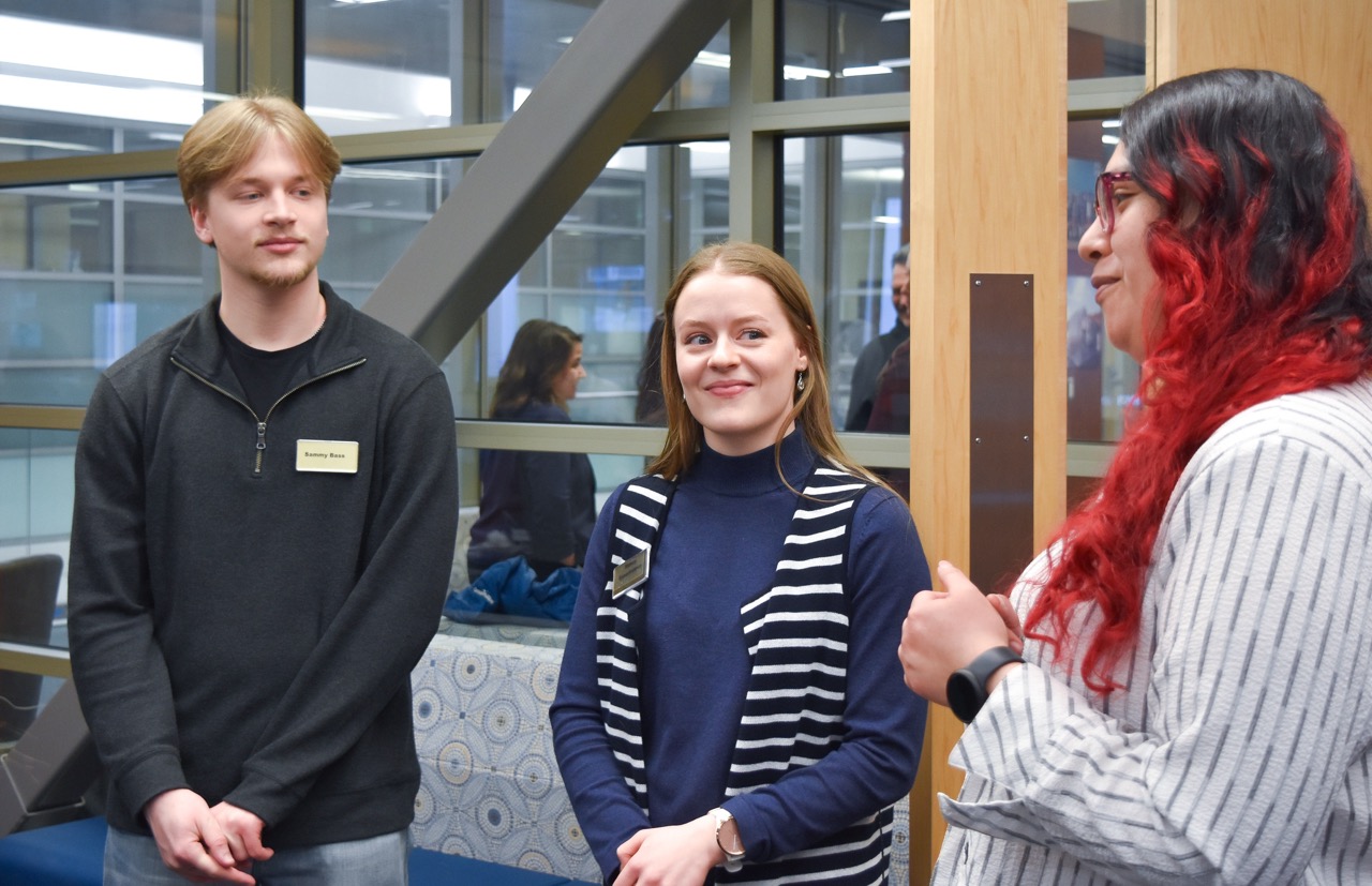 three college students stand and talk with each other in a conference room