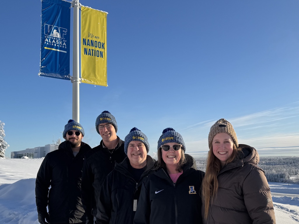 three men stand with two women on a winter day wearing coats and beanies