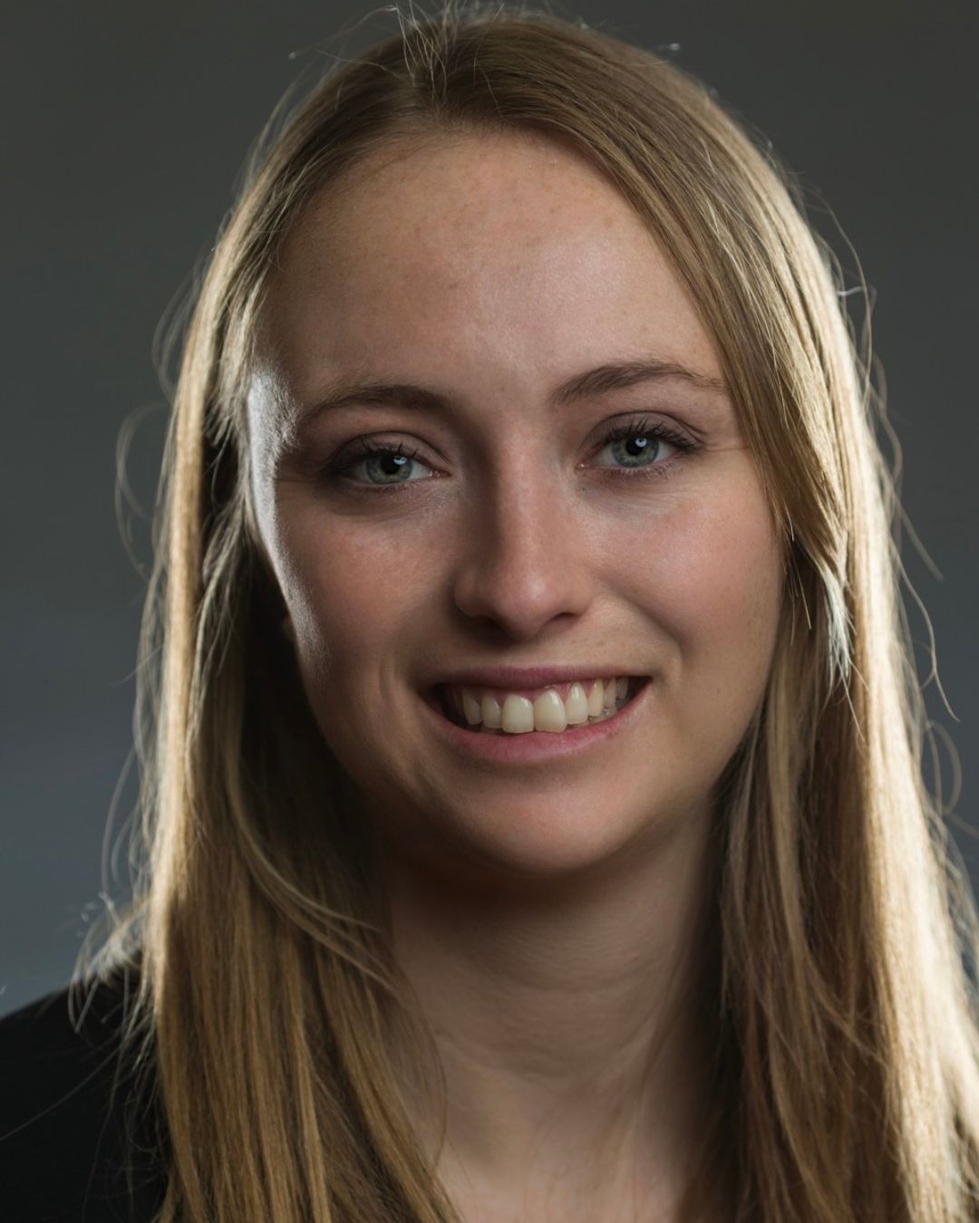 Blonde woman smiles for close up portrait with grey background