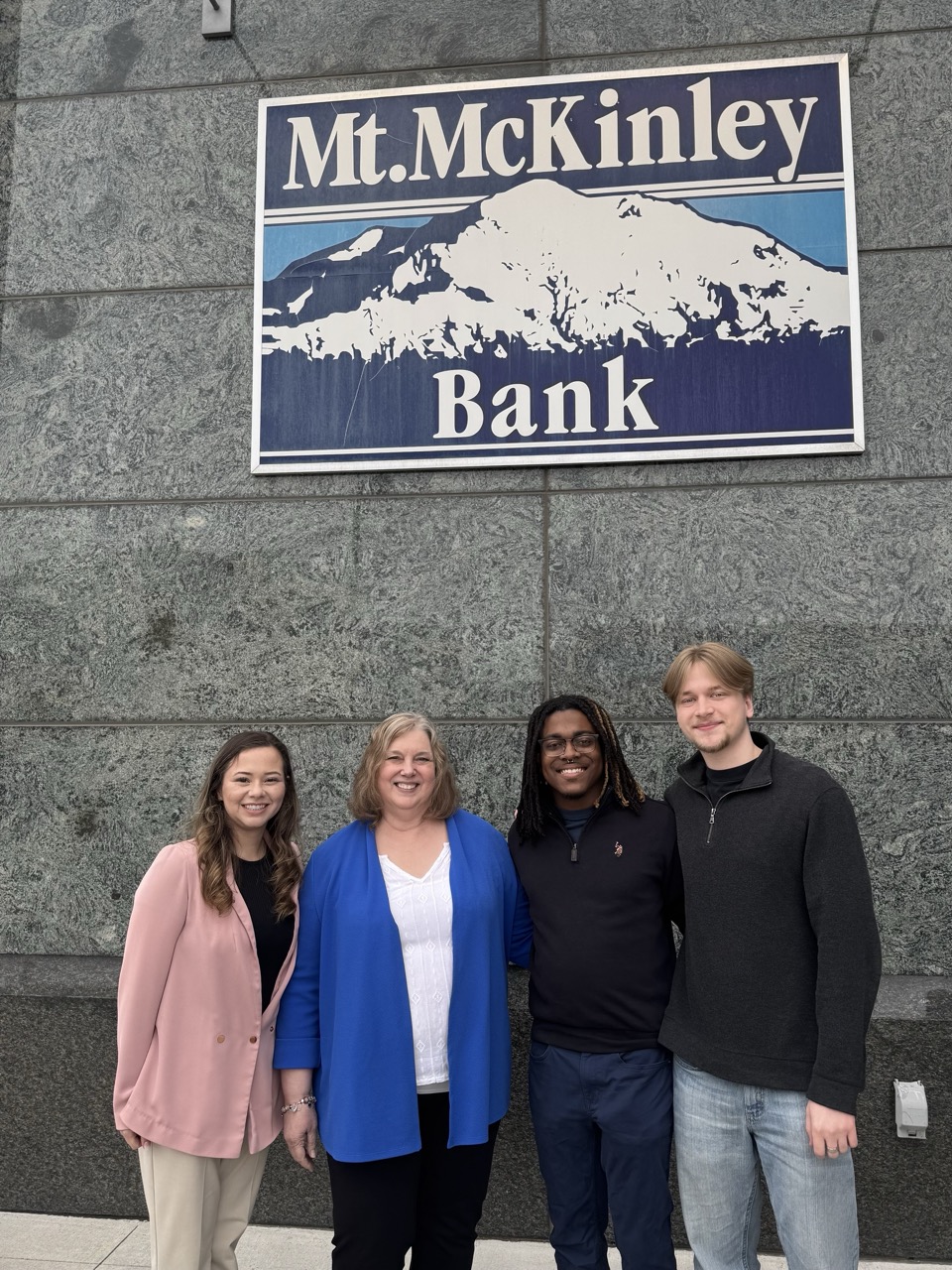 three students stand with Patty Mongold in front of Mt. McKinley Bank