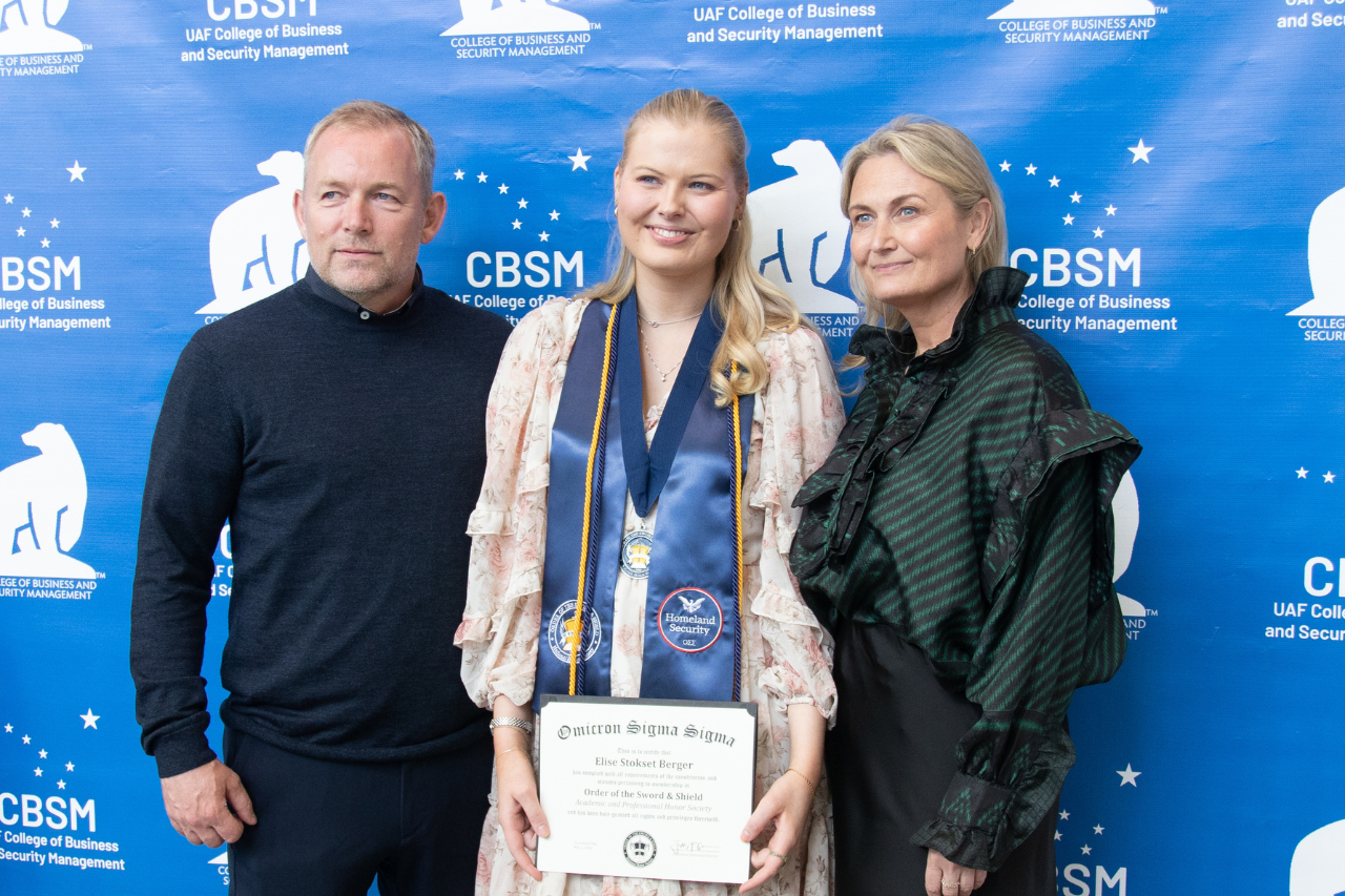 woman wears regalia and holds honor society certificate with parents