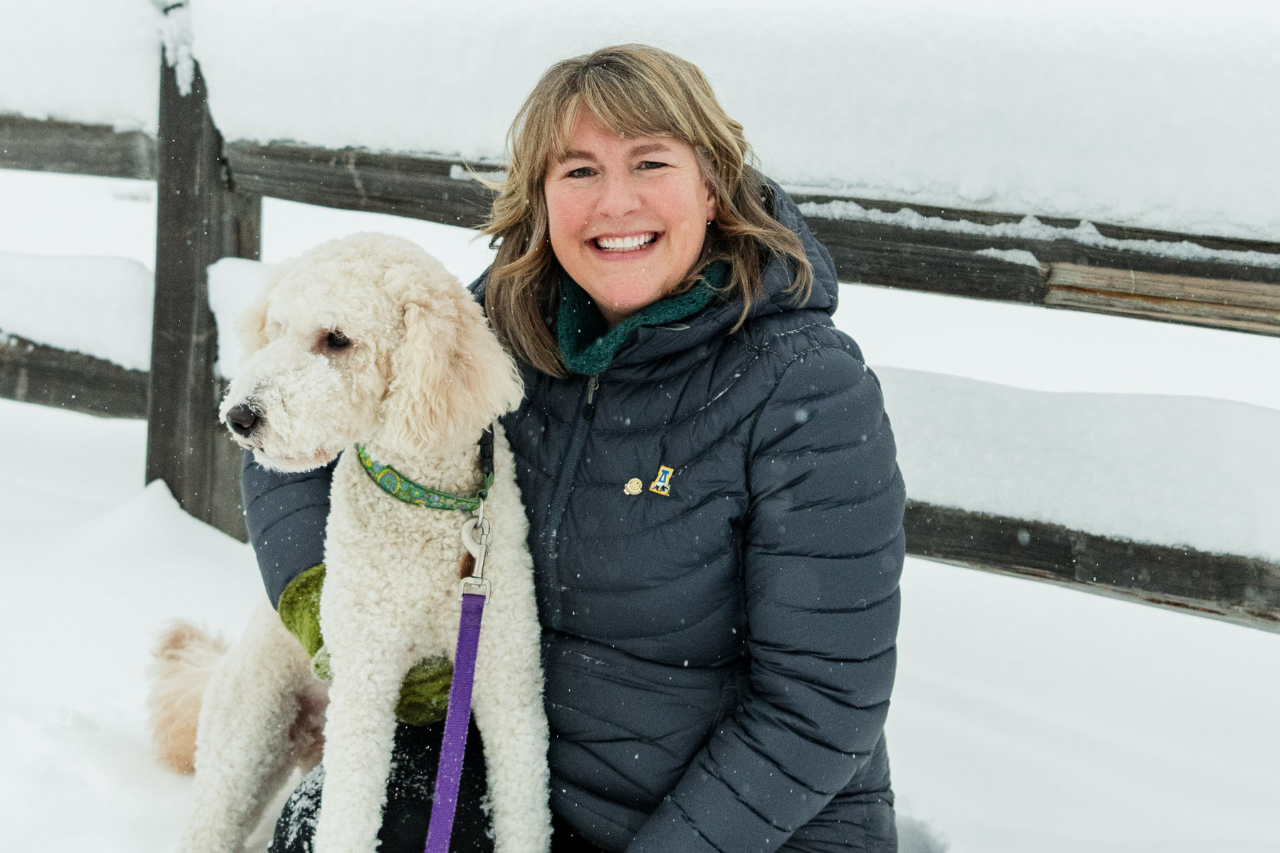 Woman smiles with dog in front of a snowy fence