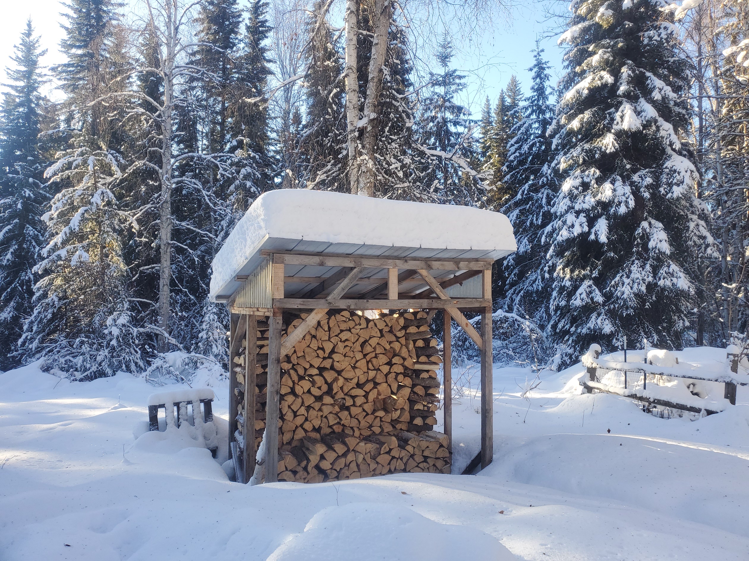 Image shows a covered wood stack in the snow.
