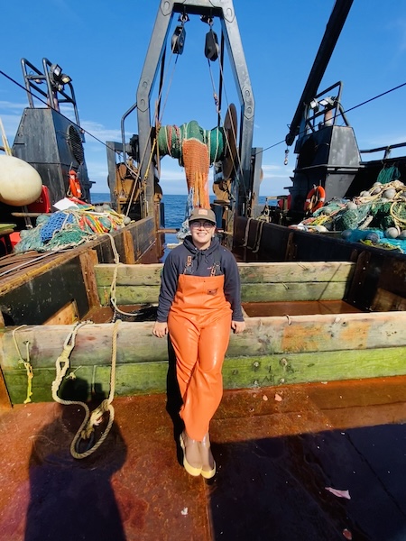 Photo of student in fish gear standing on deck of a small trawl vessel