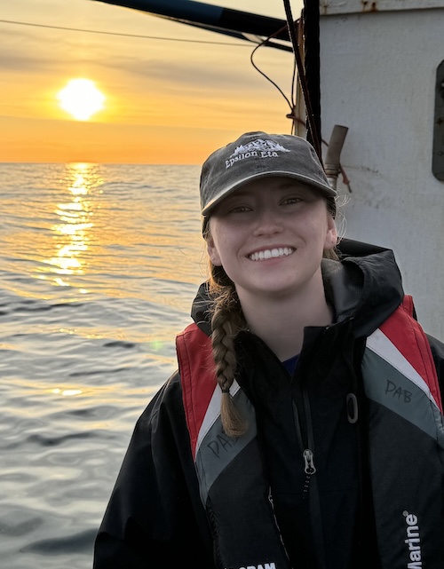 Photo of Renea on a boat with a sunset behind her