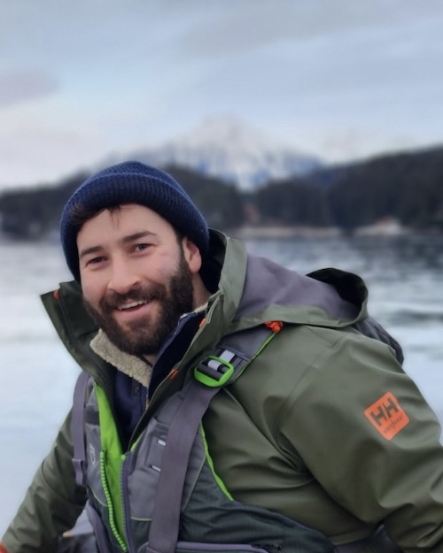 Photo of Akiva Gebler wearing heavy rain gear, driving a skiff on open water