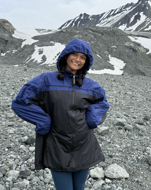 Photo of Gigi standing on a mountainside with snowcapped mountains behind her