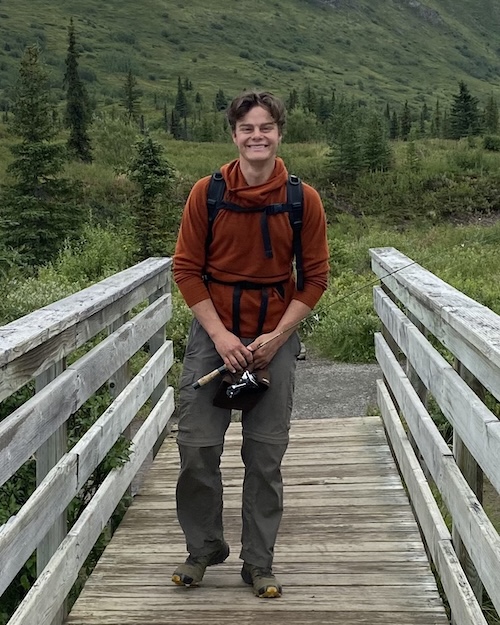 Brock Peterson walking on a bridge holding a fishing rod, with a mountain in the background